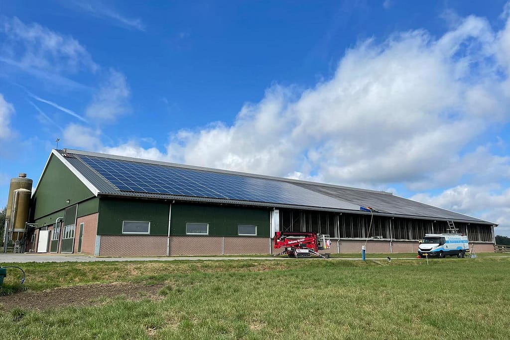 Foto van stal met dak met zonnepanelen en een groen grasveld ervoor.